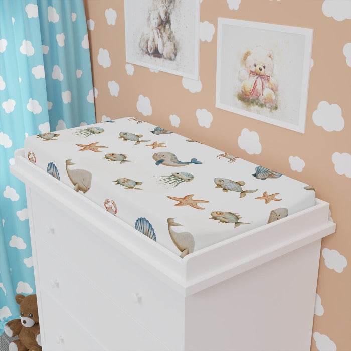 Water-resistant and durable changing pad cover featuring a serene ocean motif with whales, fish, crabs, starfish, and jellyfish illustrations, against a white background, blending functionality with a love for the sea in baby's nursery.