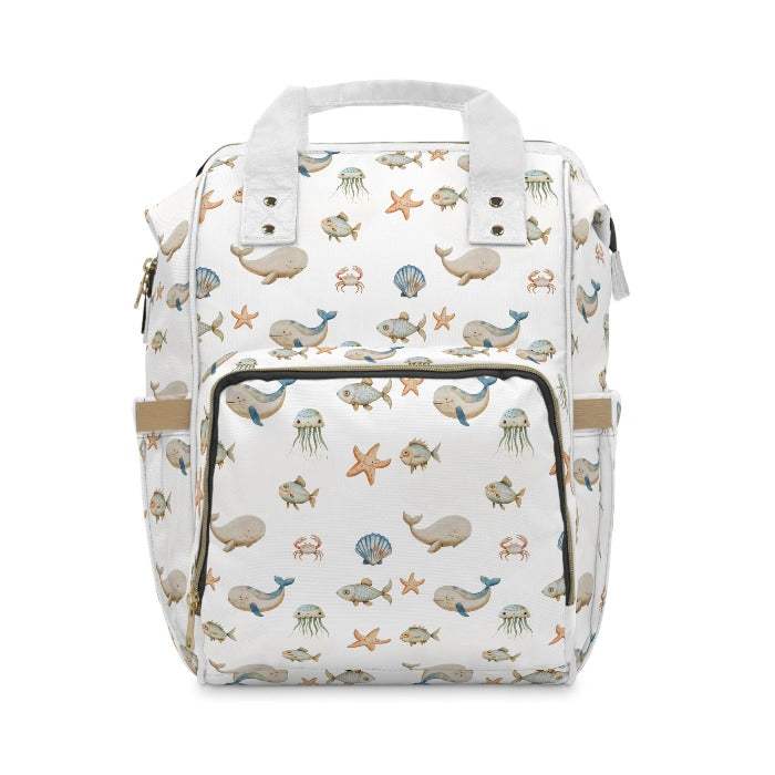 Marine life-inspired diaper backpack set against a pure white background, featuring detailed depictions of whales, fish, crabs, starfish, and jellyfish, ideal for organized and stylish parents.