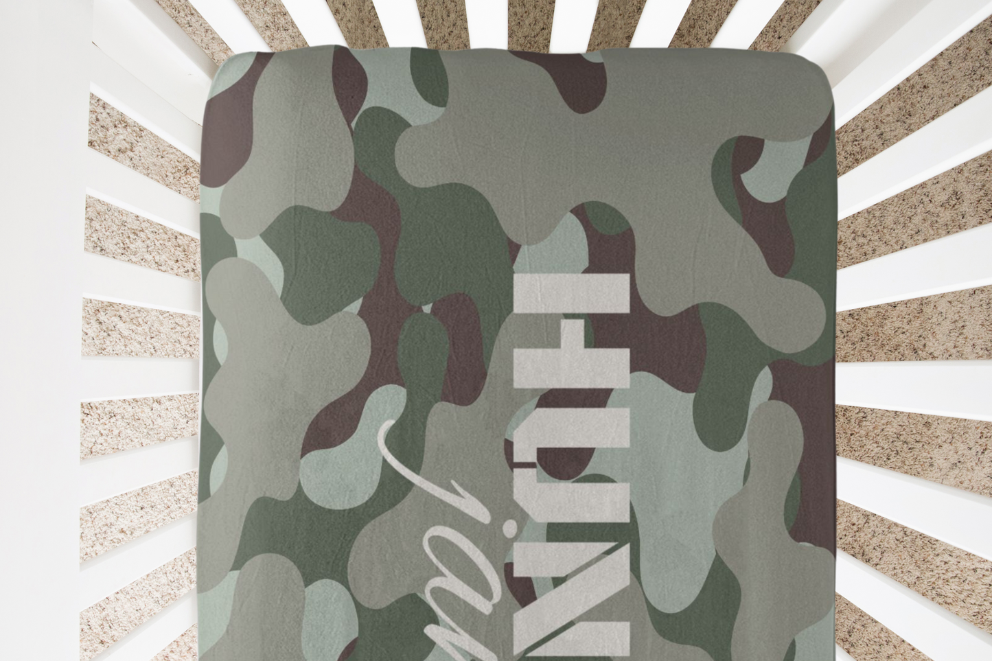 A soft, durable baby crib sheet featuring a seamless camouflage pattern, blending shades of green, brown, and beige, perfect for adding a touch of adventure to your nursery decor.